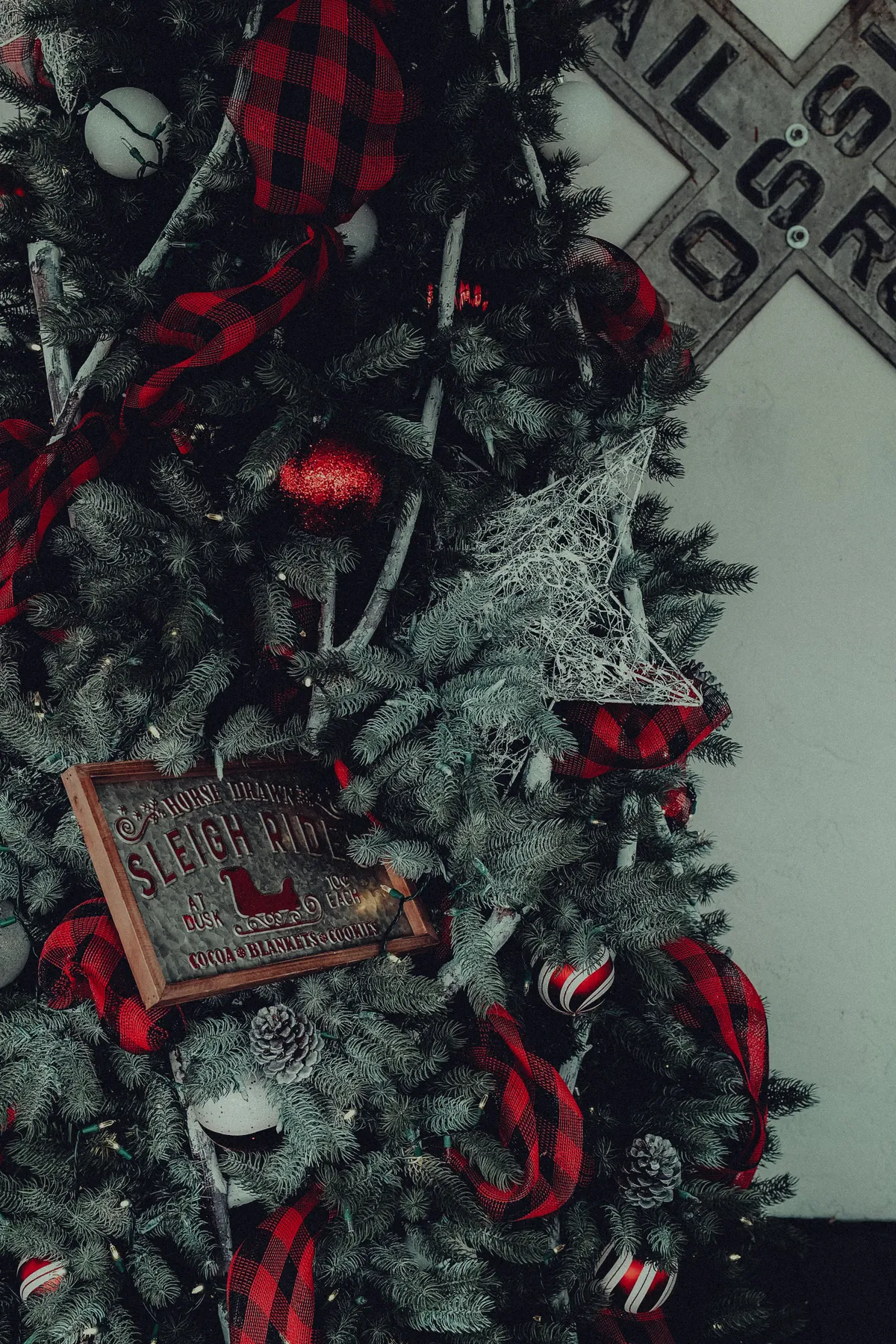 A beautifully decorated Christmas tree with ornaments and a vintage sleigh ride sign indoors.