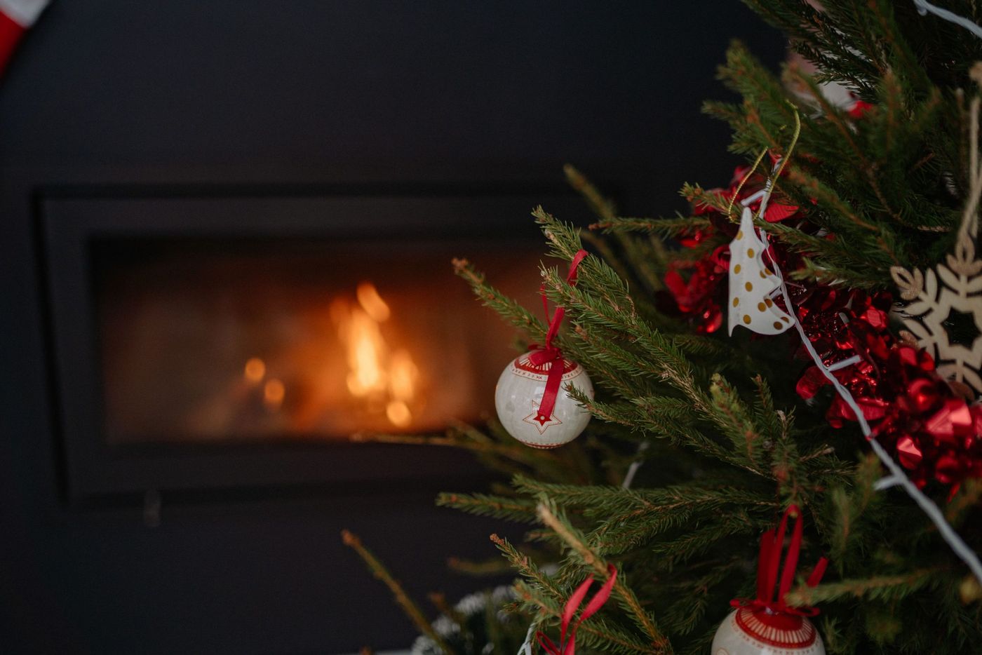 A Christmas tree adorned with ornaments in front of a warm fireplace, creating a festive atmosphere.