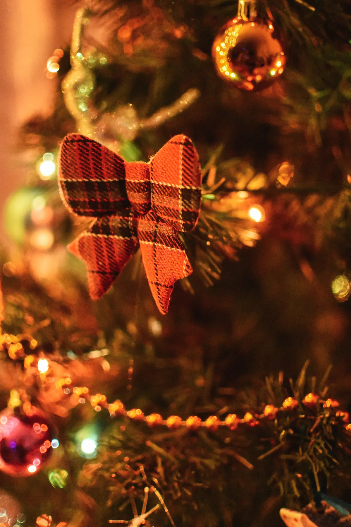 A close-up of a decorative bow and ornaments on a lit Christmas tree, creating a cozy holiday ambiance.