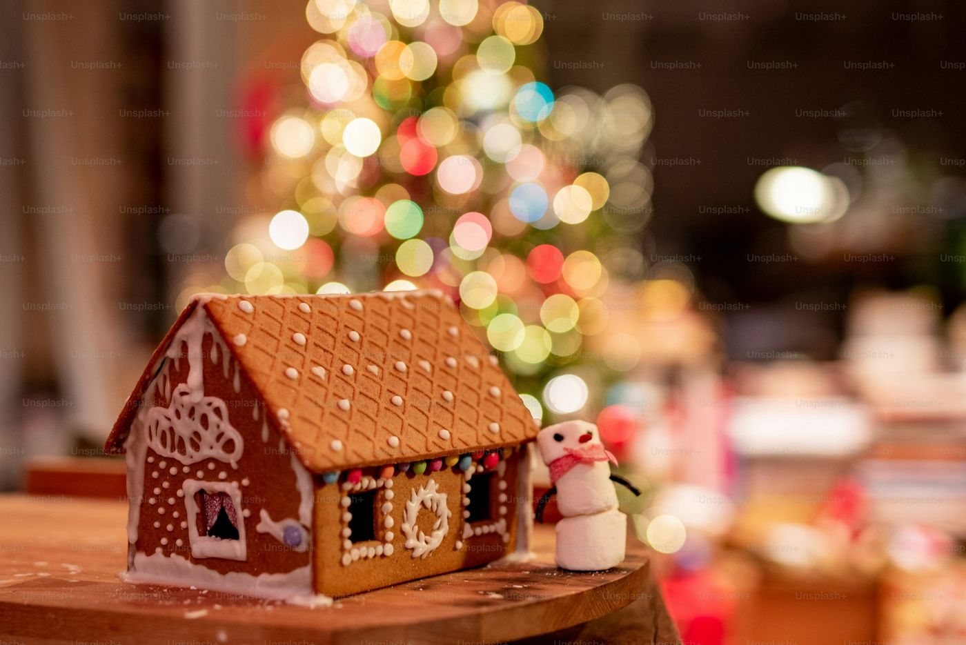 A gingerbread house with a christmas tree in the background - Photo on  Unsplash+