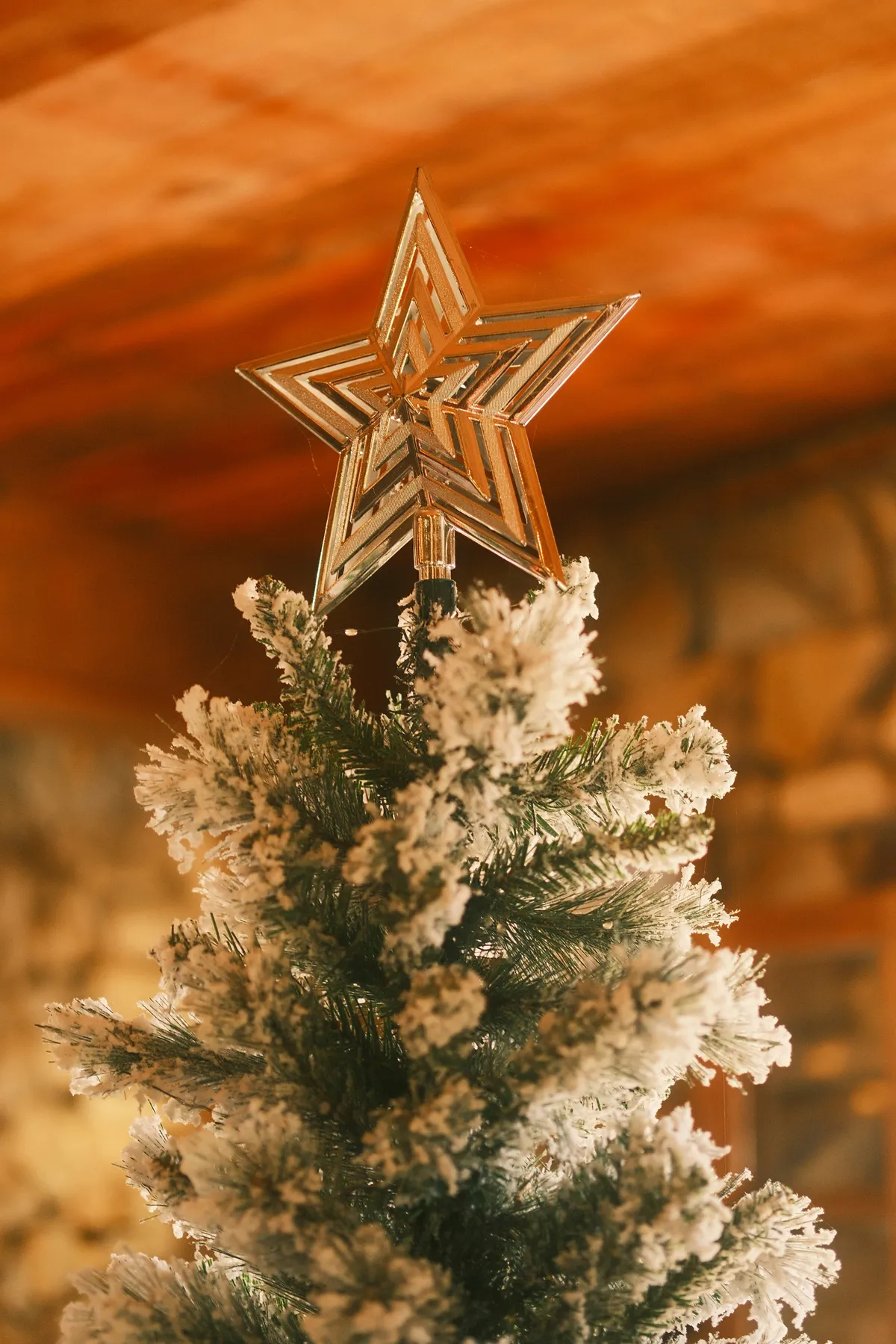 A gold star tree topper on a flocked Christmas tree in a warm room