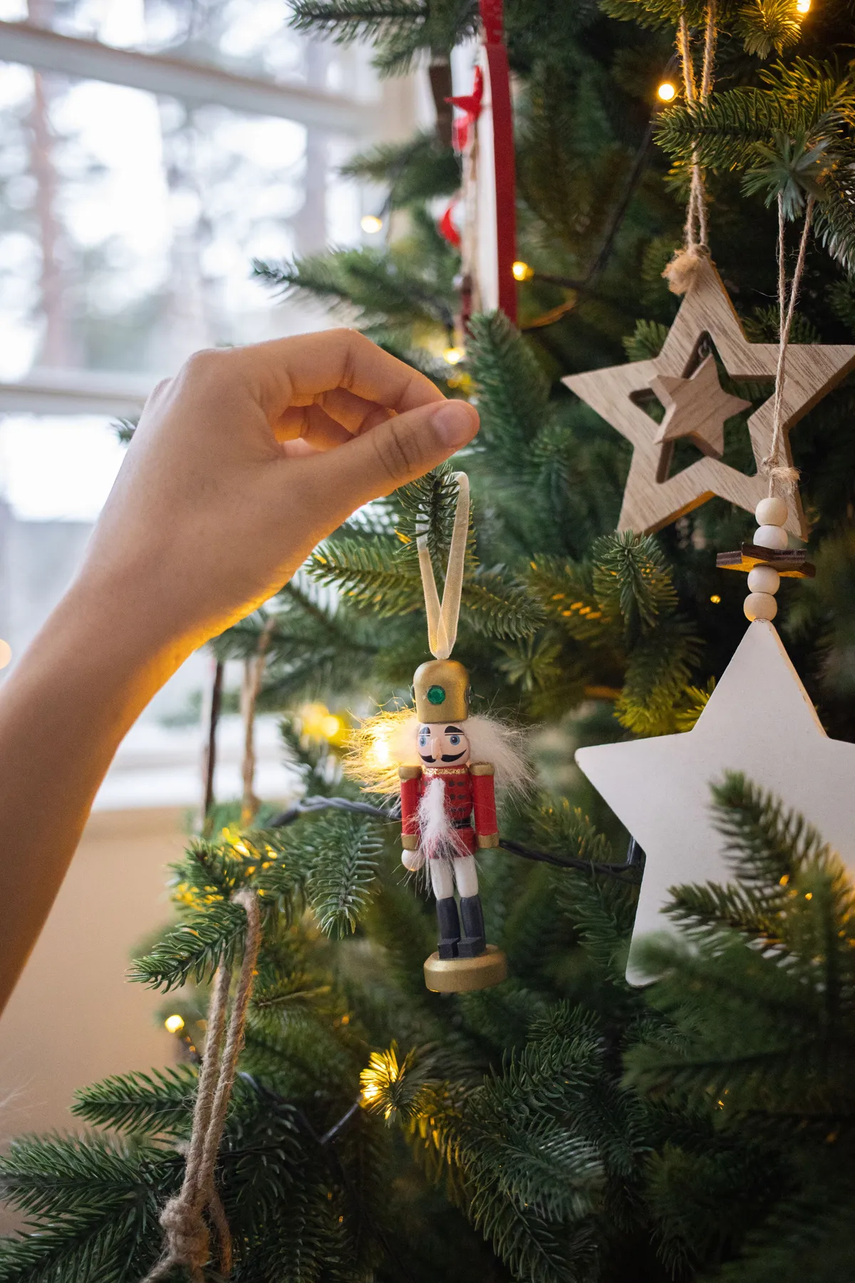 A person decorates a Christmas tree with a nutcracker ornament, capturing a festive and traditional holiday scene.