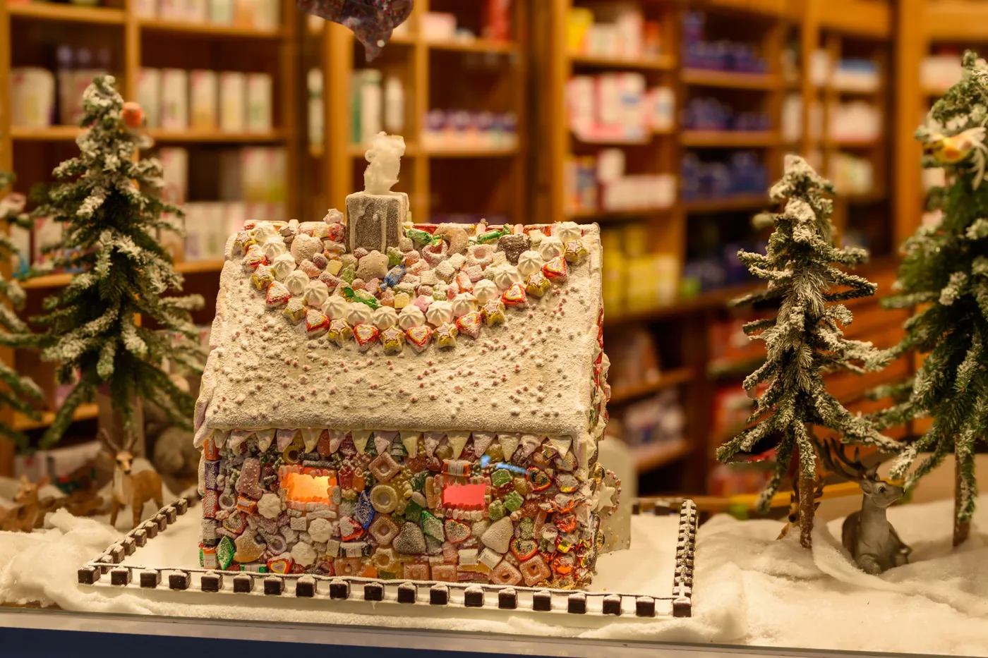 Charming gingerbread house adorned with candy surrounded by snow-dusted trees in a winter wonderland setting.