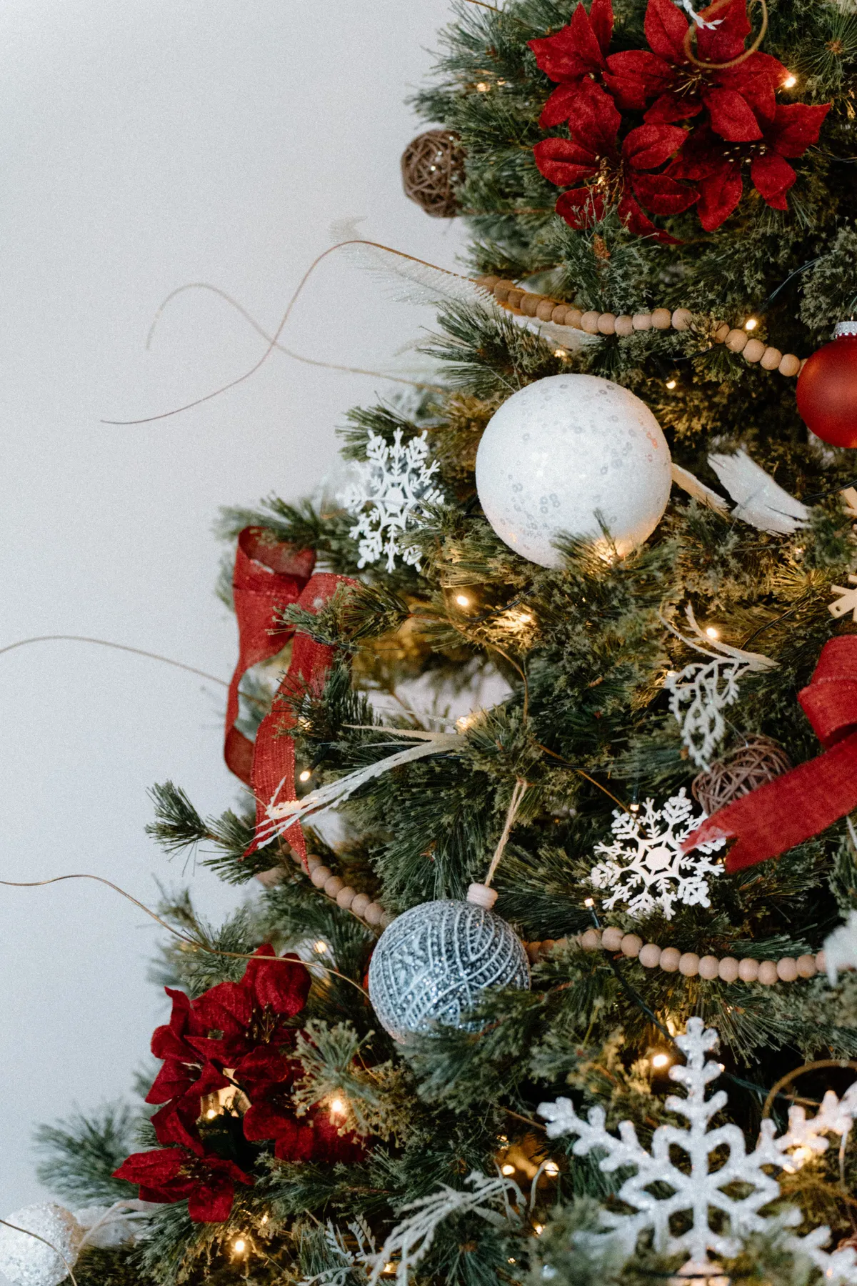 Close-up of a beautifully adorned Christmas tree with ornaments, snowflakes, and red ribbons.