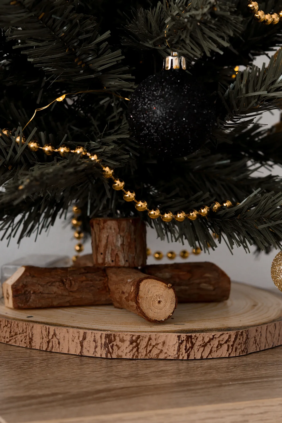 Close-up of a Christmas tree adorned with a black bauble and golden decorations on a wooden base.