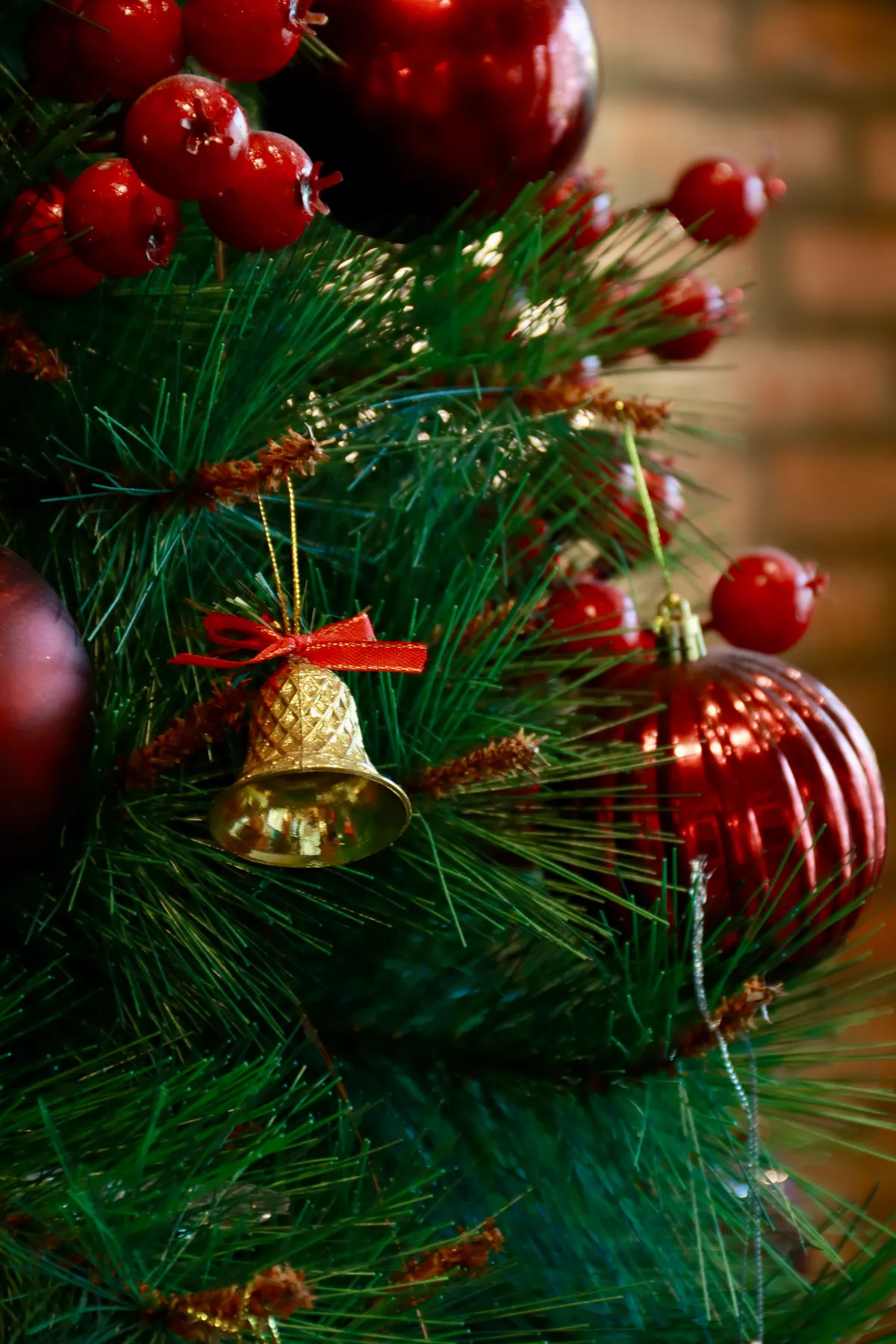 Close-up of a decorated Christmas tree with red baubles and a golden bell ornament, evoking holiday cheer.