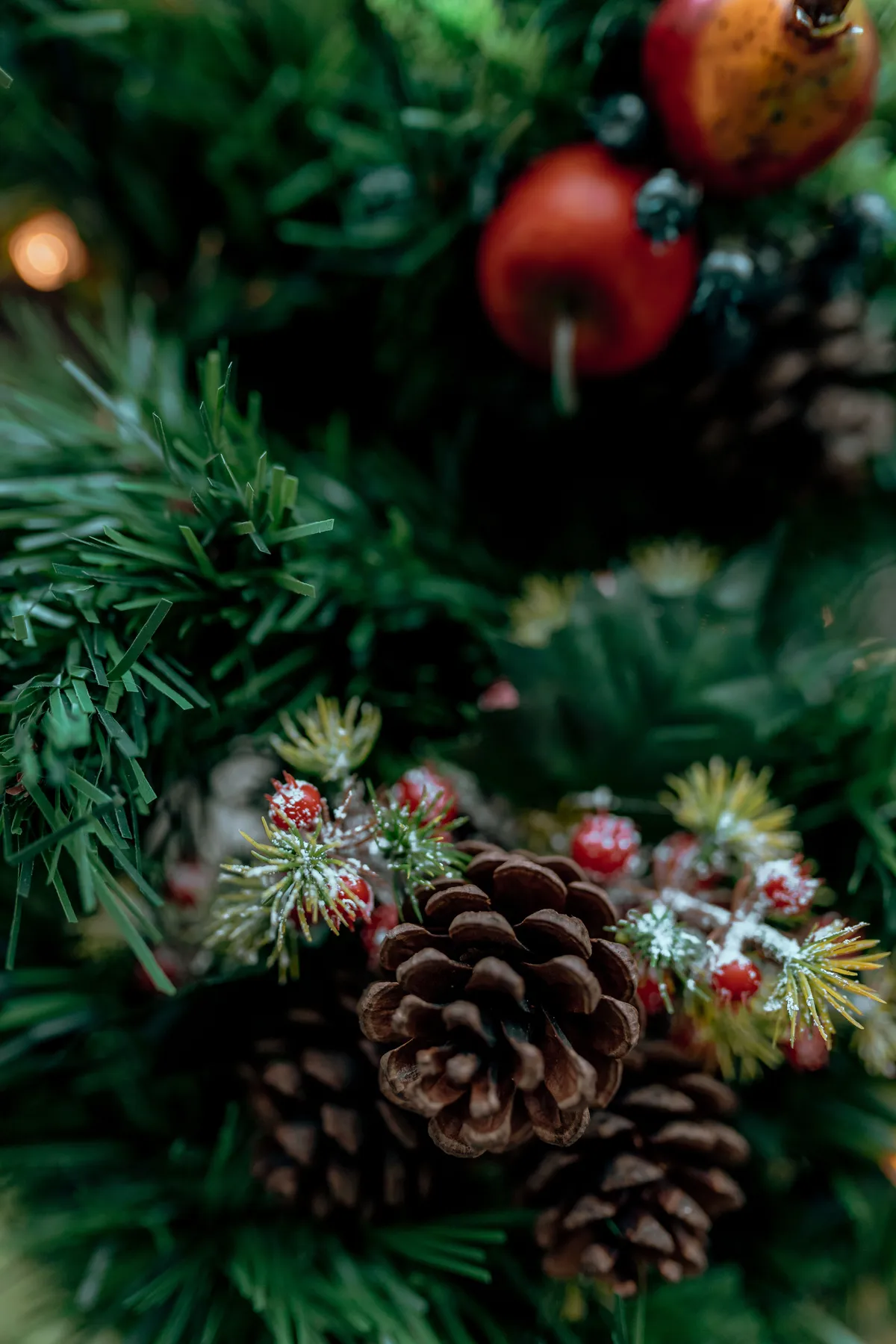 Close-up of a decorated Christmas tree with pine cones, berries, and faux apples, evoking holiday spirit.
