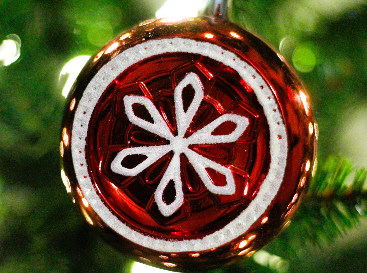 Close-up of a shimmering red Christmas ornament with white design hanging on a tree.