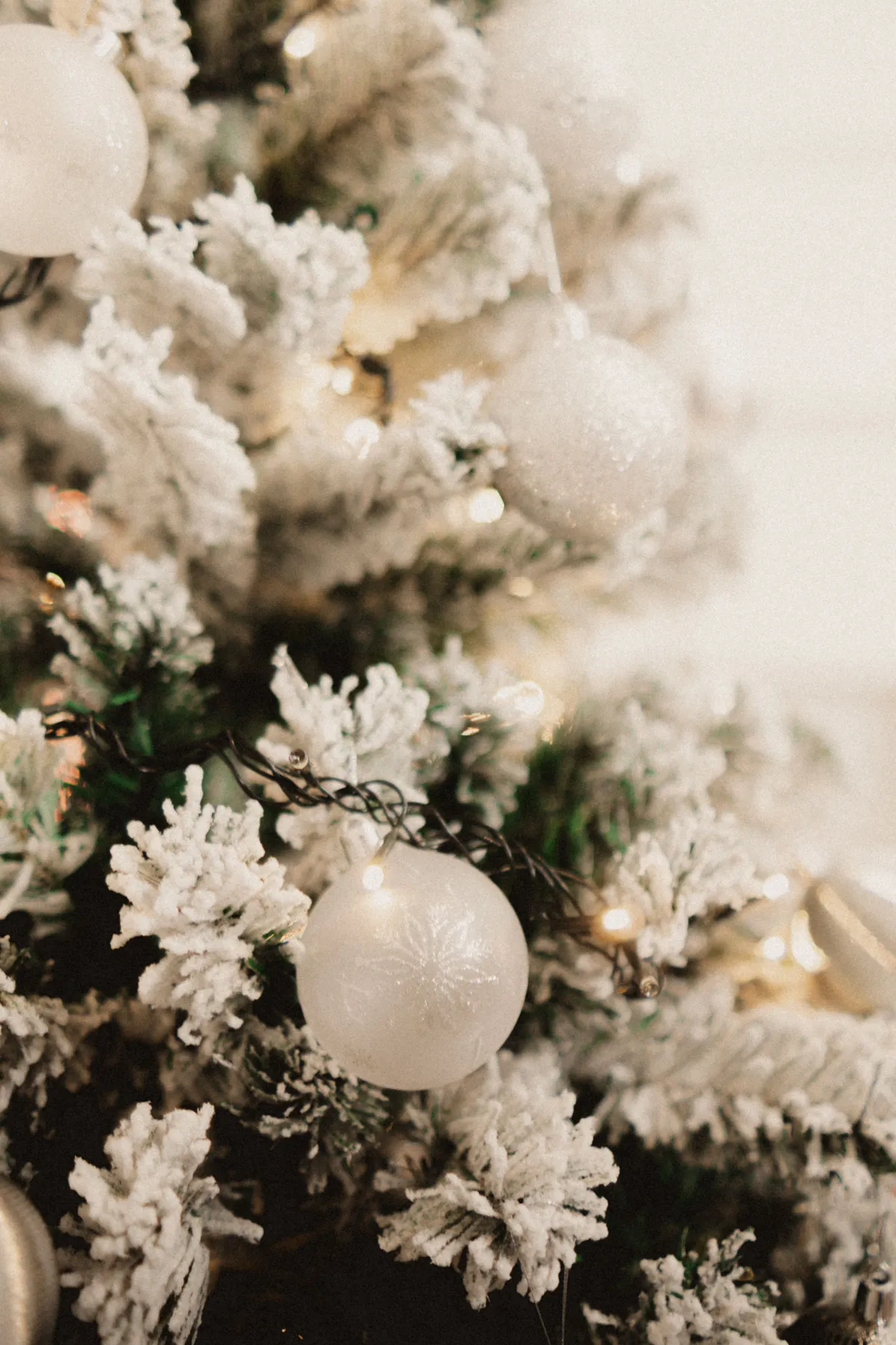 Close-up of a snowy Christmas tree decorated with white baubles and lights, evoking festive spirit.