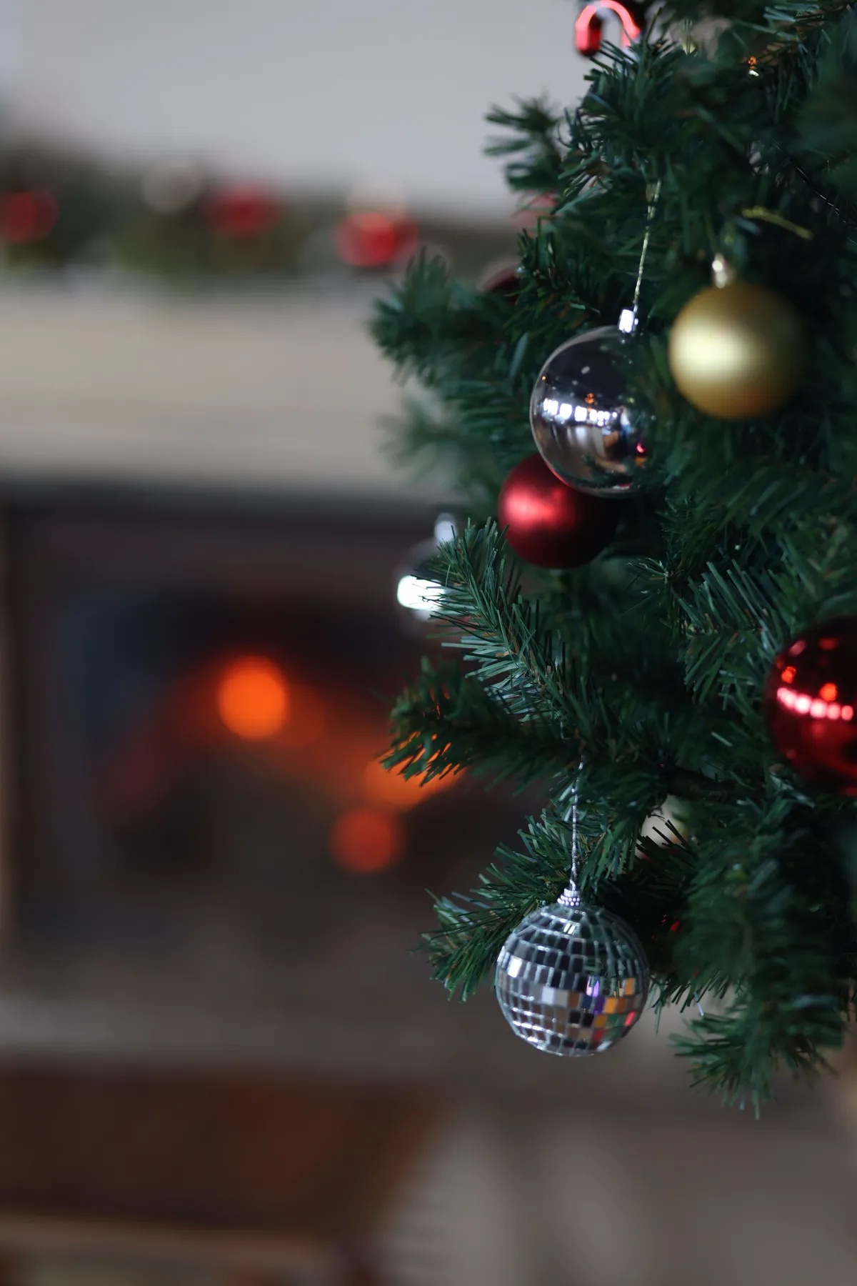 Cozy Christmas tree decorated with baubles near a warm fireplace.