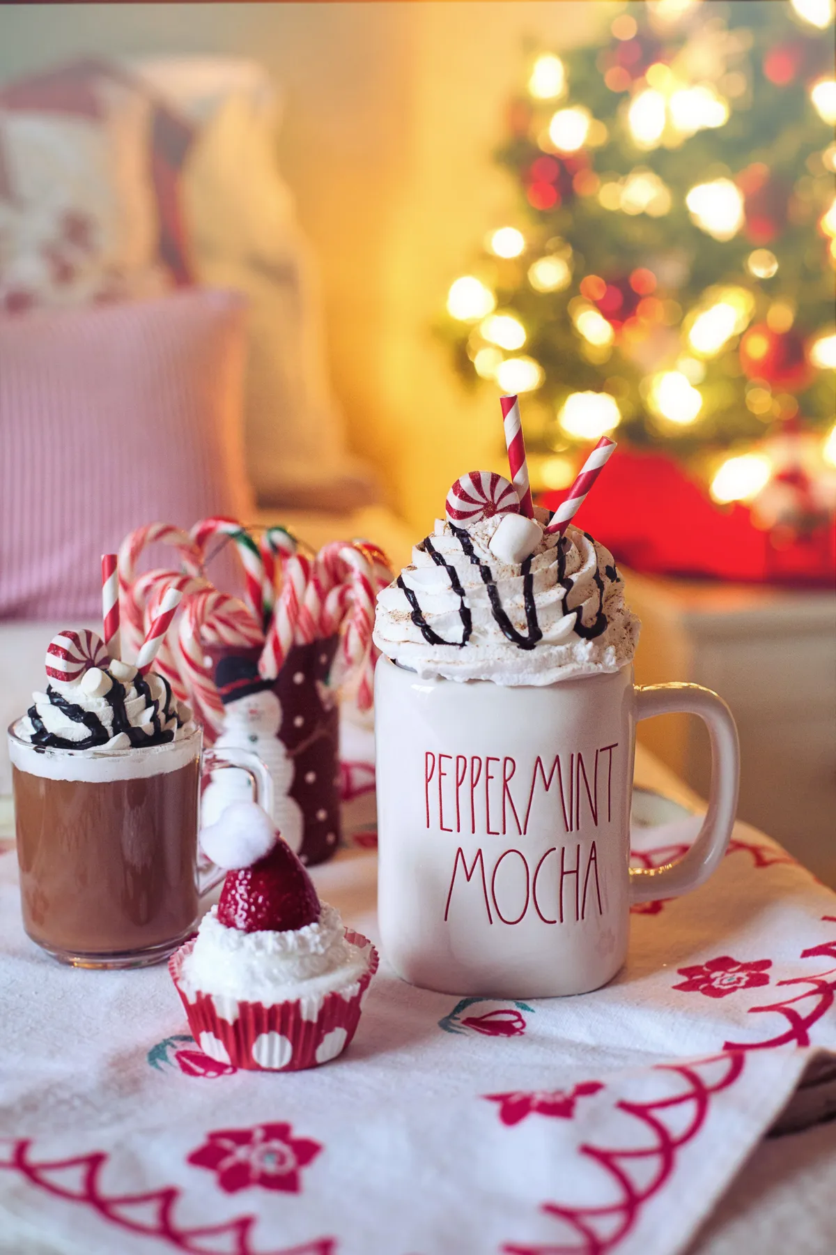 Cozy holiday scene featuring peppermint mocha, cupcakes, and Christmas tree.