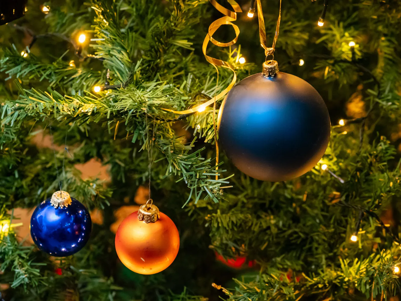Decorative blue and orange baubles on a lit Christmas tree branch.