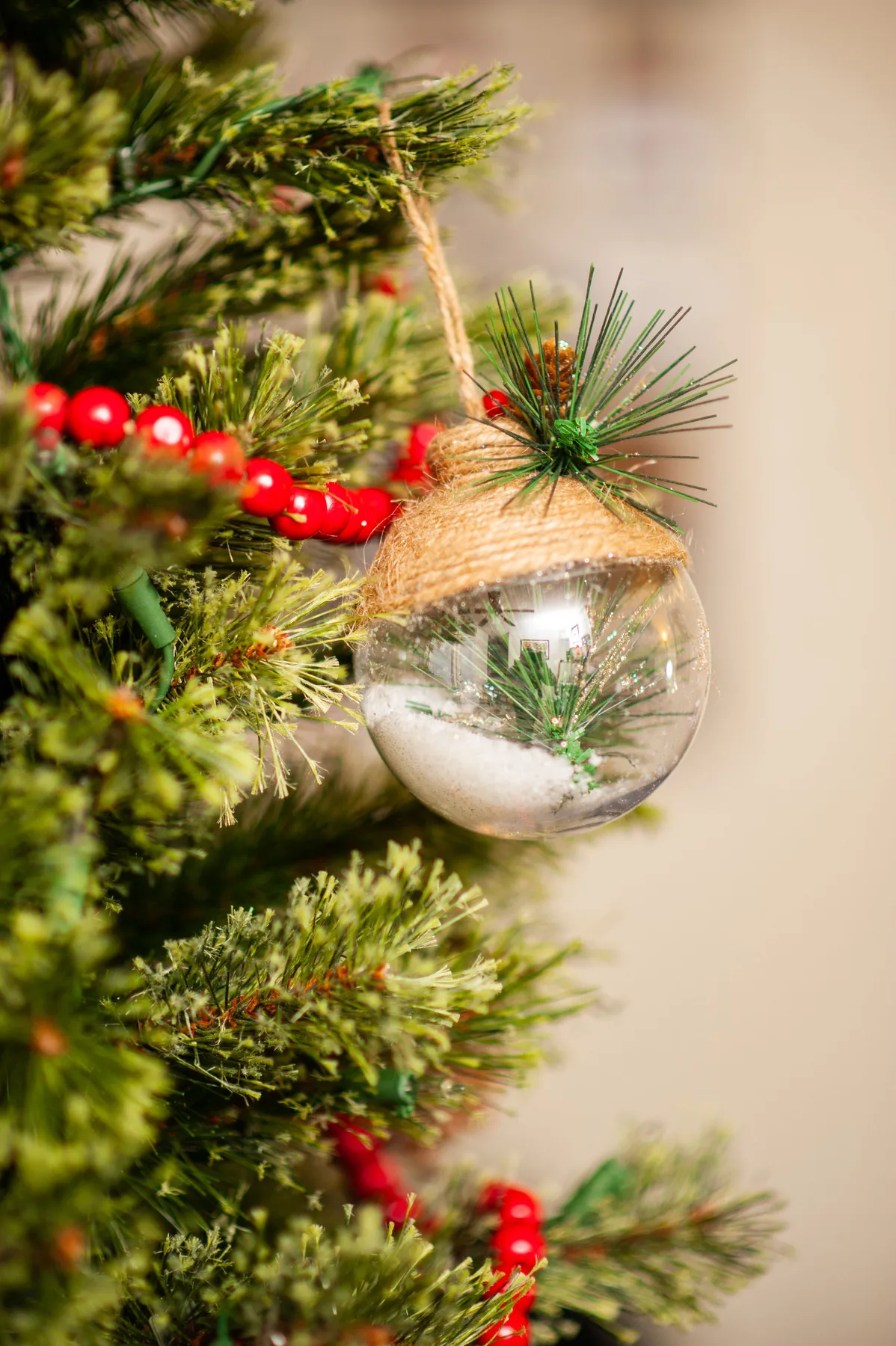 Festive Christmas tree close-up featuring a transparent ornament with greenery and red beads.