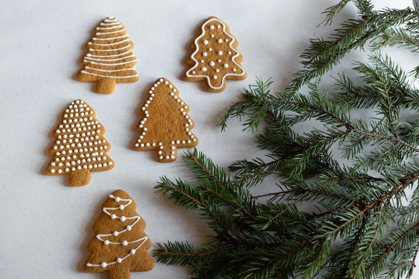 Five decorated gingerbread cookies shaped like Christmas trees with pine sprigs.