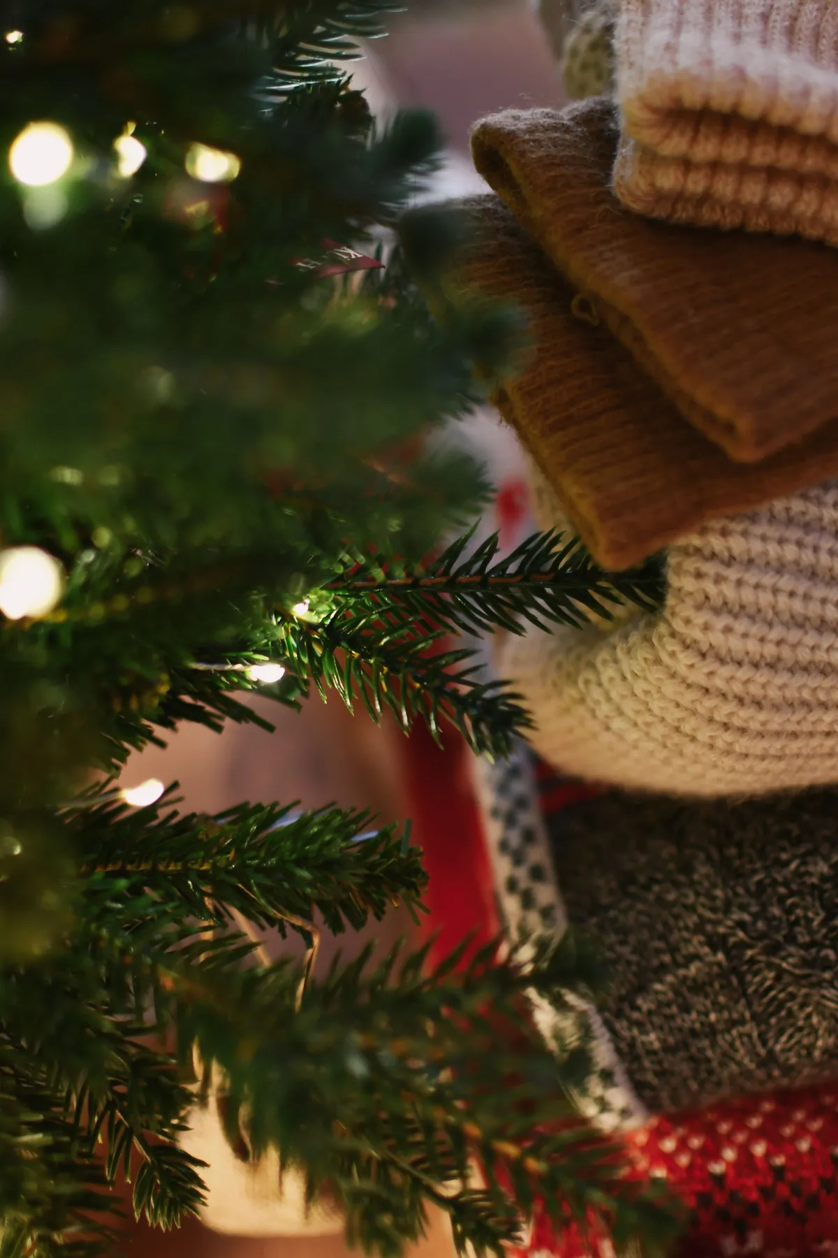 Stack of cozy sweaters next to a Christmas tree, perfect for holiday warmth.