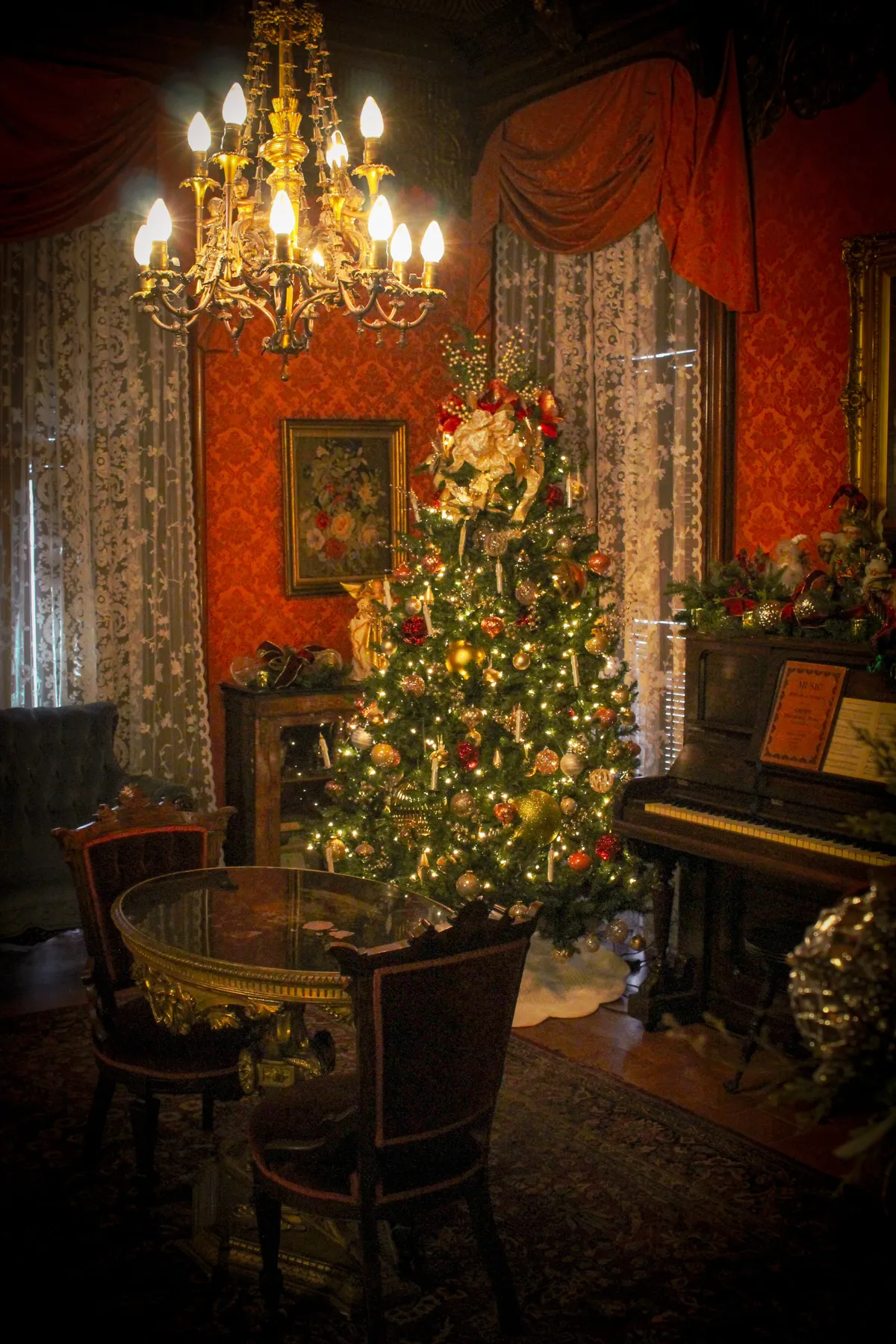 Vintage Victorian interior with a decorated Christmas tree, chandelier, and grand piano.