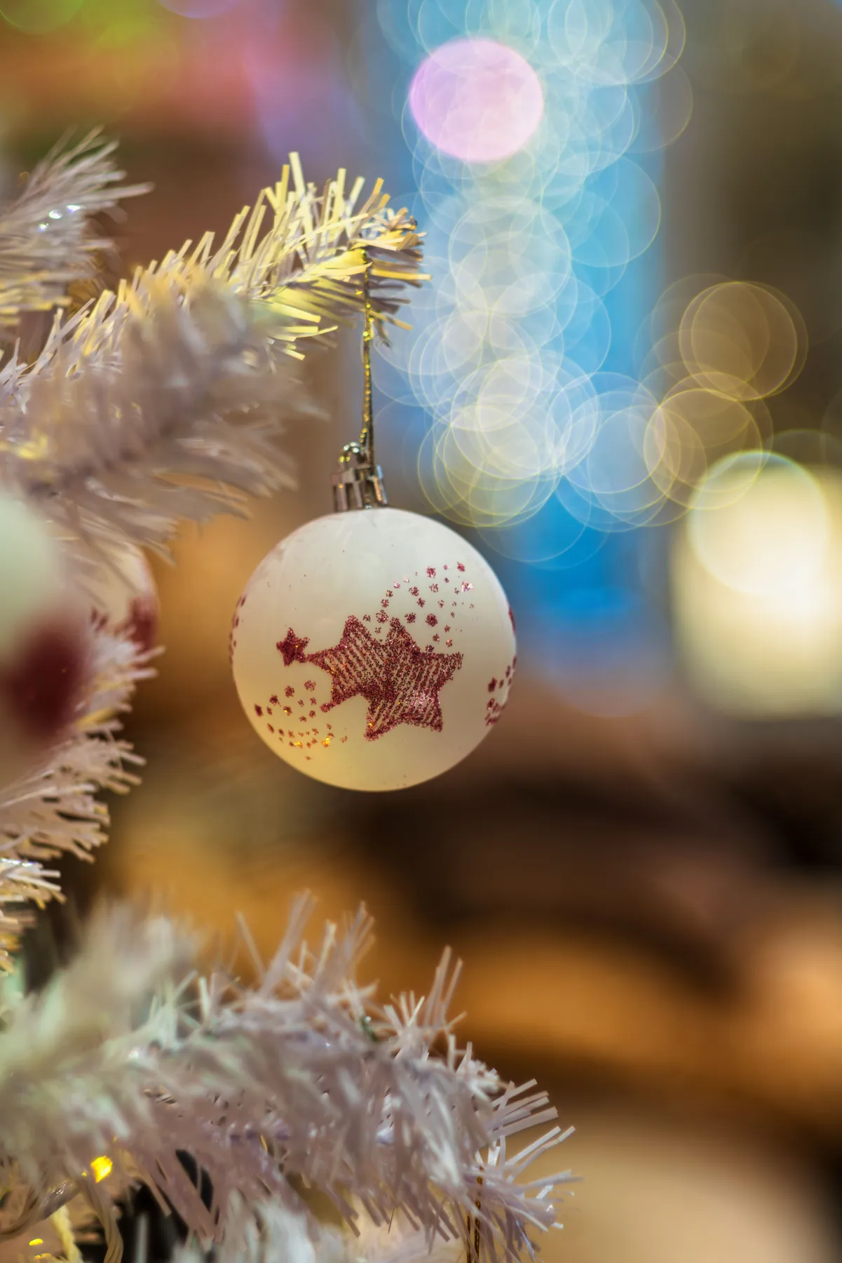 White Christmas ornament with red stars on a tree, blurred lights background.